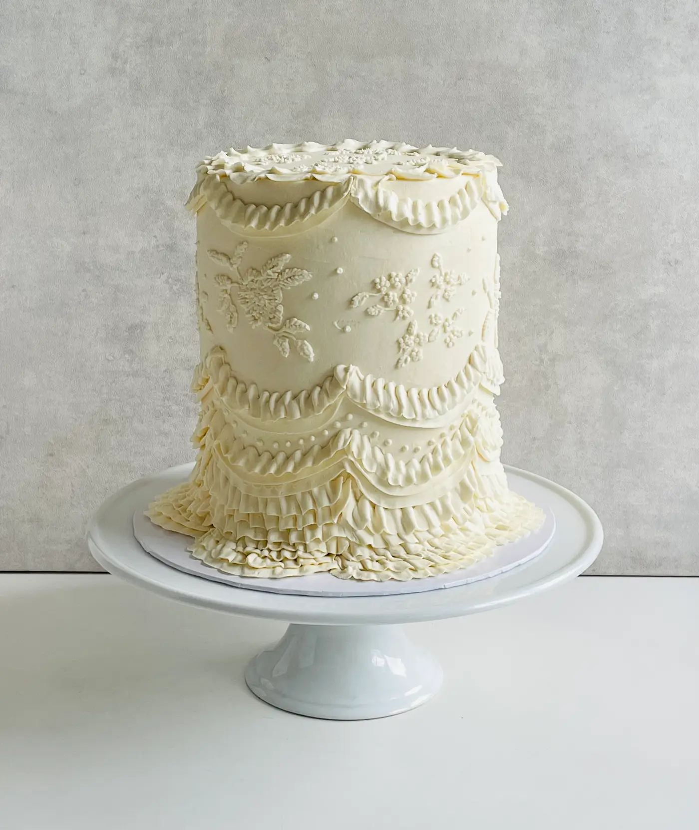 A tall ivory Lambeth cake piped with buttercream lace, ruffles and florals