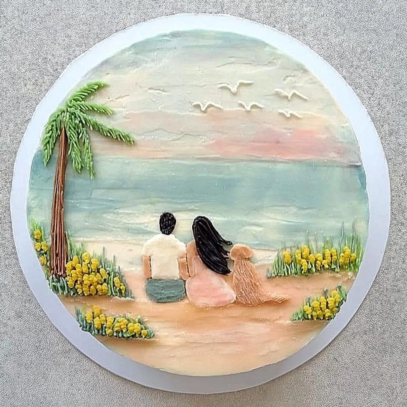 A hand-painted cake of a couple watching the sunset from a beach